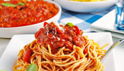 A white plate of crockpot spaghetti sauce on pasta with bowls of sauce and spaghetti in the background.