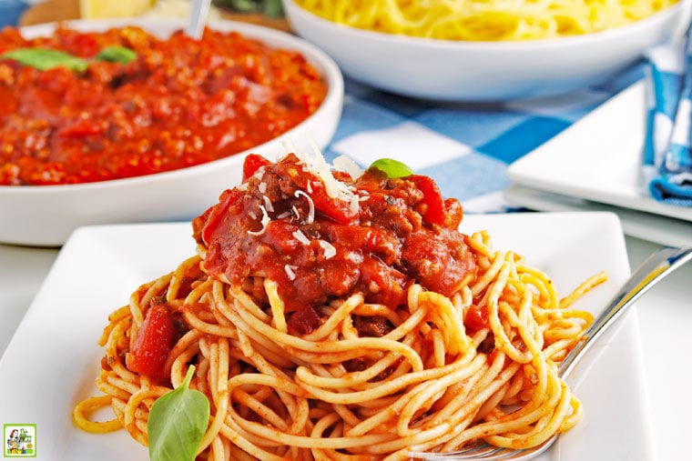 A white plate of crockpot spaghetti sauce on pasta with bowls of sauce and spaghetti in the background.