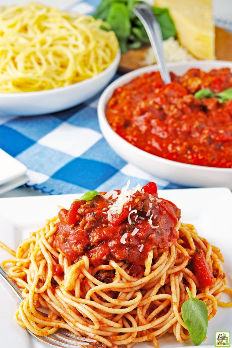 Closeup of a plate of slow cooker spaghetti sauce on a pile of spaghetti with bowls of sauce and spaghetti in the background.
