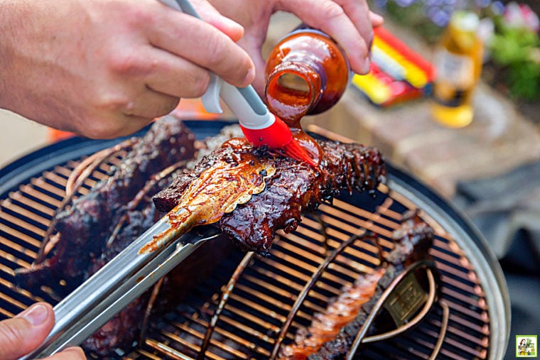 Brushing BBQ sauce on racks of pork ribs during grilling.