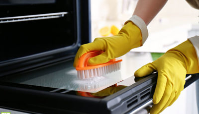 Woman wearing yellow rubber gloves cleaning oven with baking soda and scrub brush.
