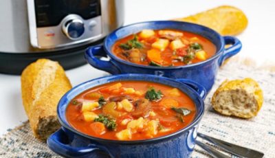 Two blue bowls of vegetable soup with bread, spoon, and an Instant Pot.