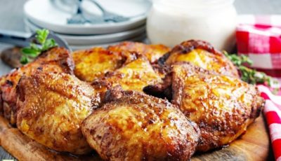 Smoked chicken thighs on a wooden cutting board with plates, forks, sauce, and napkins.