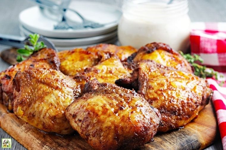 Smoked chicken thighs on a wooden cutting board with plates, forks, sauce, and napkins.