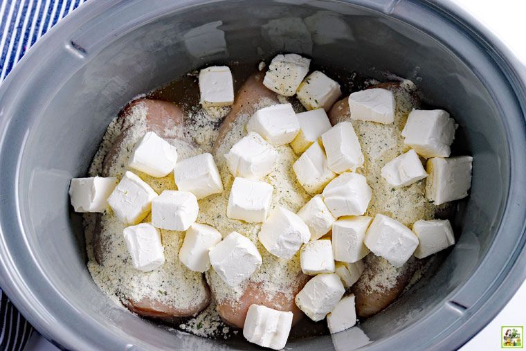 Making crock pot crack chicken in a slow cooker with cream cheese cubes on chicken breasts with ranch seasoning mix.