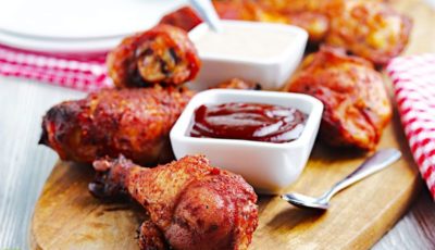 Smoked chicken drumsticks on a wooden board with small bowls of BBQ sauce.