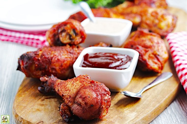 Smoked chicken drumsticks on a wooden board with small bowls of BBQ sauce.