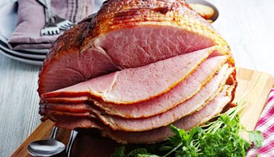 Traeger smoked ham on a wooden cutting board with serving utensils, napkins, and garnish.