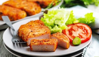 Traeger smoked pork chops on a plate with fork, lettuce, and sliced tomato.