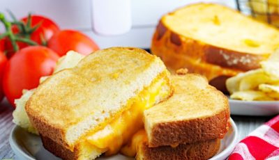 Air fryer grilled cheese sandwiches on a white plate with a red napkin and tomatoes in front of an air fryer.