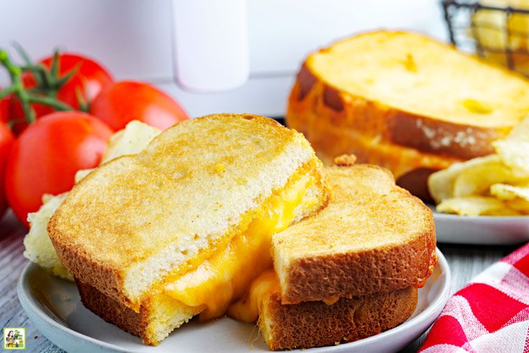 Air fryer grilled cheese sandwiches on a white plate with a red napkin and tomatoes in front of an air fryer.