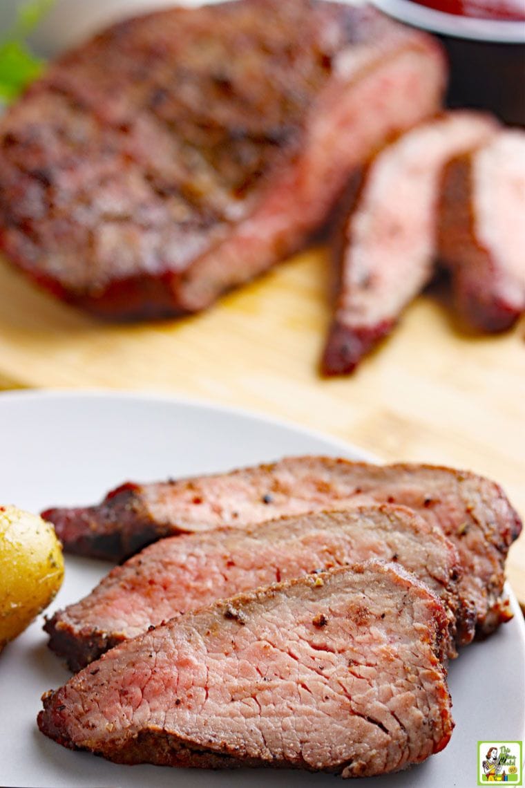 Slices of smoked tri-tip roast on a gray plate with roast in the background.