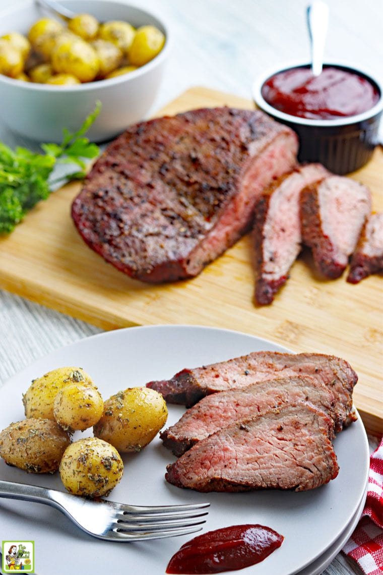 Smoked beef roast on a cutting board, sliced tri-tip and roasted potatoes on a plate, and bowls of potatoes and BBQ sauce.