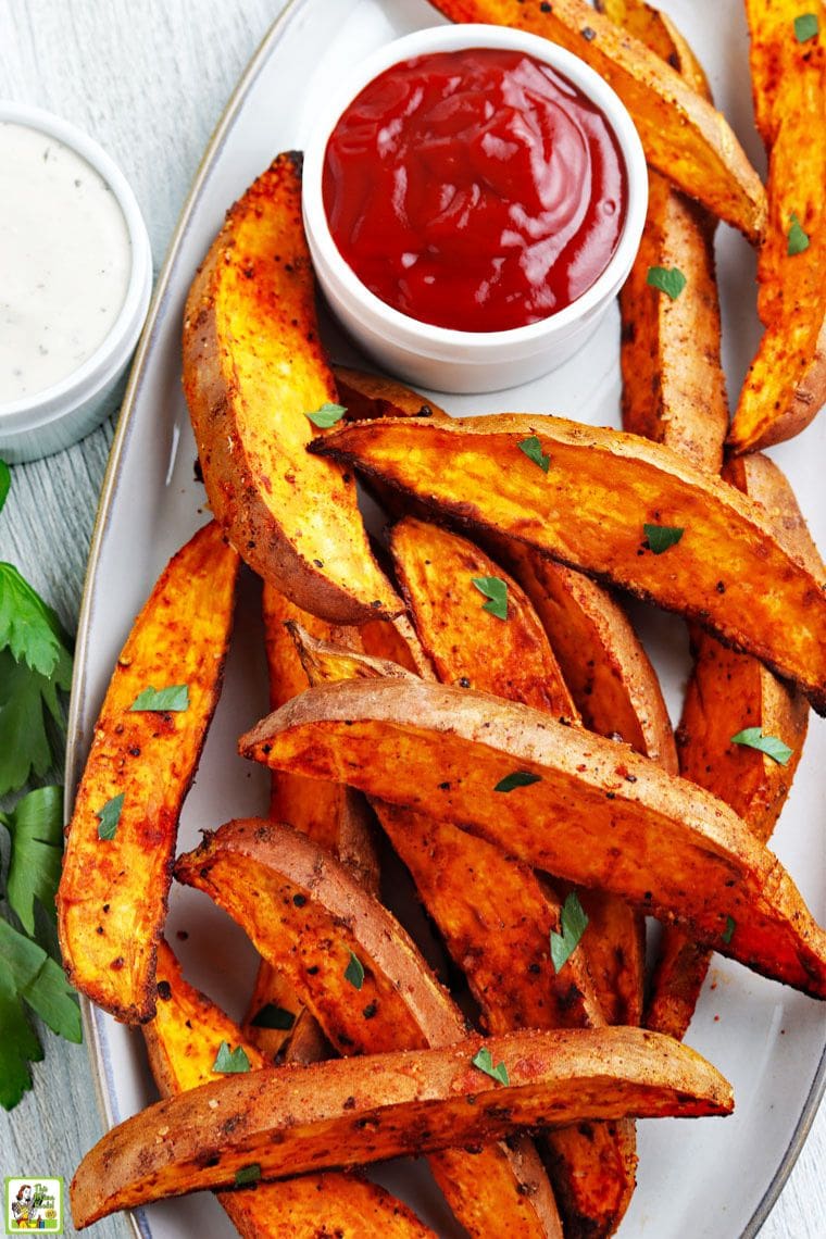 Overhead view of a platter of air-fried sweet potato wedges with small bowls of ketchup and Alabama sauce. 