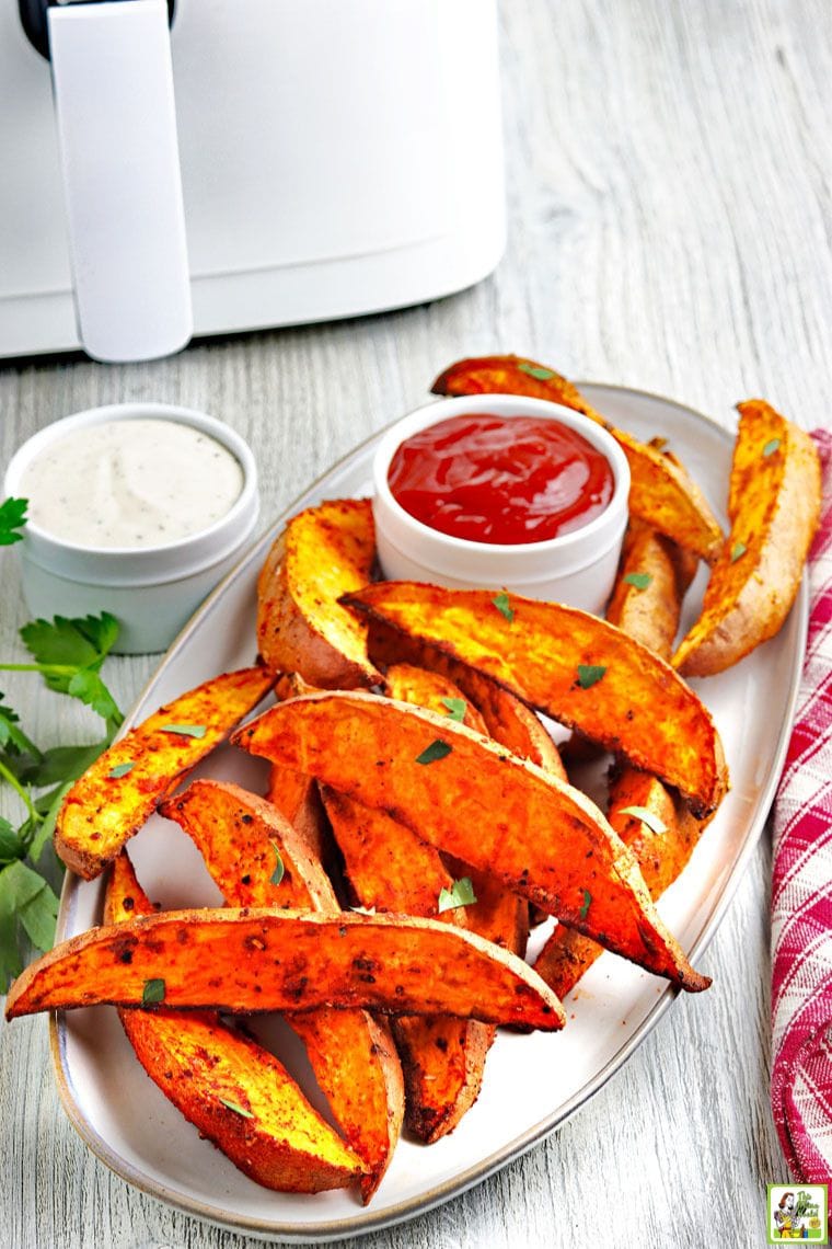 A tray of fried sweet potatoes, two small bowls of dipping sauce, and an air fryer in the background.