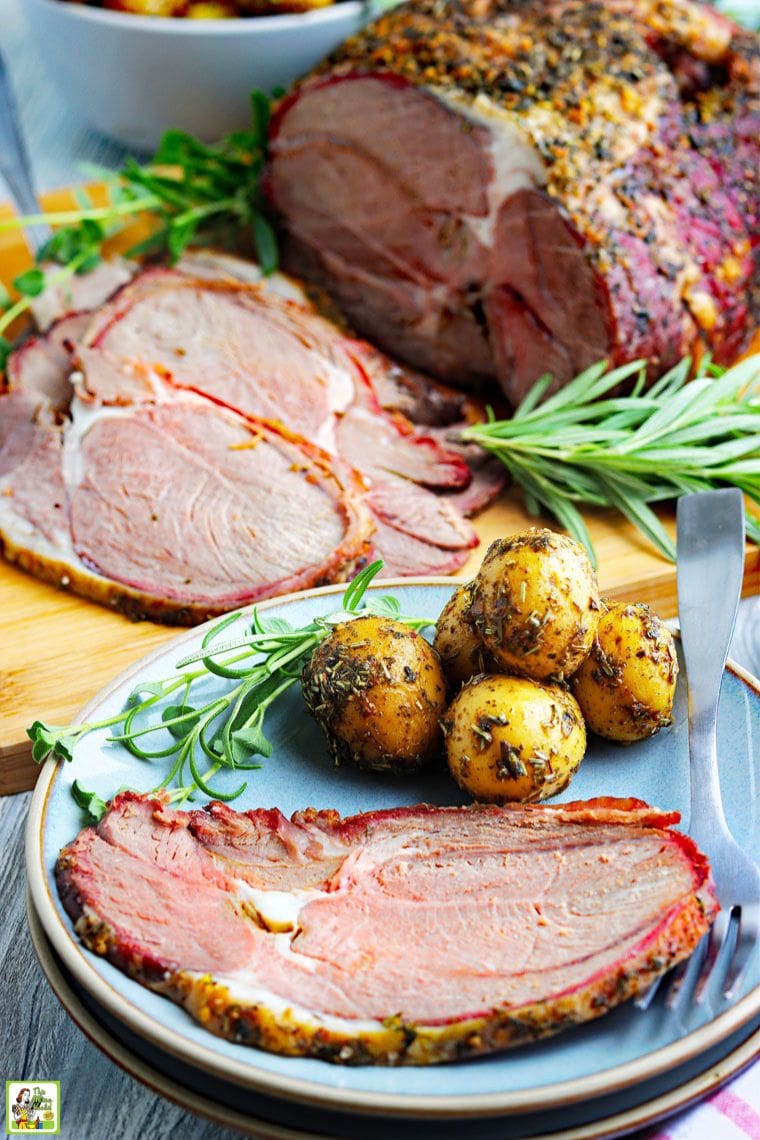 A plate of sliced smoked lamb with potatoes with more sliced roasted lamb in the background garnished with fresh herbs.